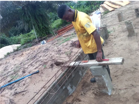A young builder levelling a reinforced concrete foundation beam at the New Cess school site